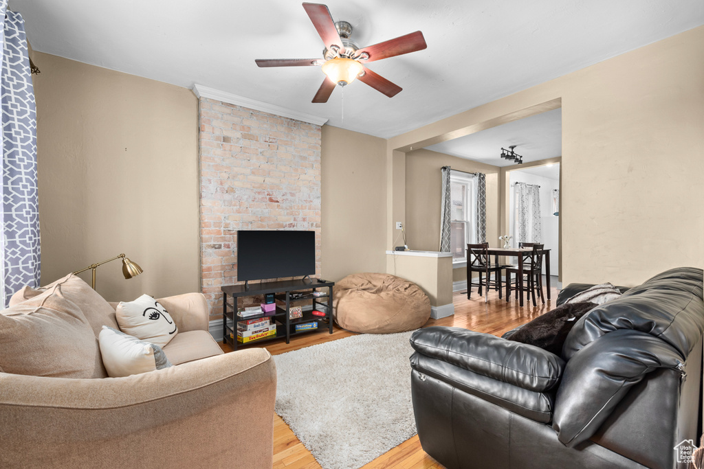 Living room with light wood-type flooring, brick wall, a fireplace, and ceiling fan