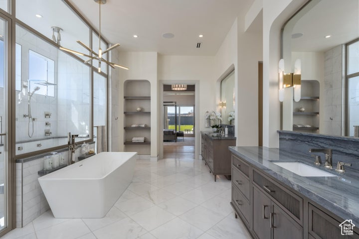Bathroom featuring tile walls, a bath, an inviting chandelier, large vanity, and tile flooring