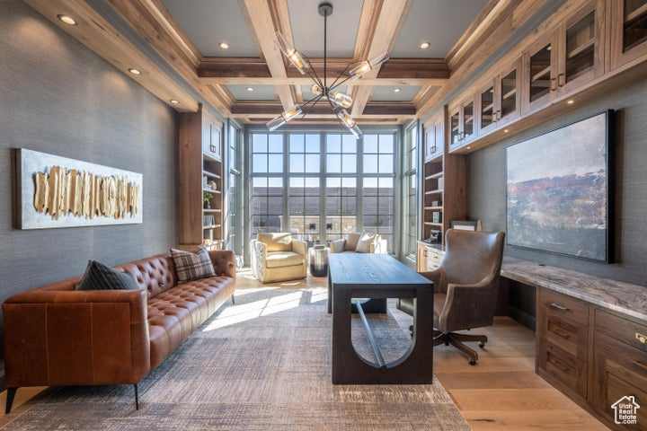 Home office with a towering ceiling, a chandelier, beam ceiling, light hardwood / wood-style flooring, and coffered ceiling