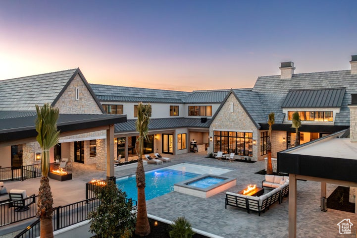 Back house at dusk with a patio, a pool with hot tub, and an outdoor living space with a fire pit