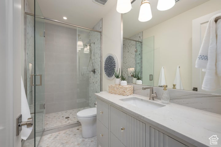Bathroom with a notable chandelier, vanity with extensive cabinet space, toilet, walk in shower, and tile flooring