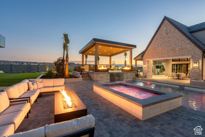 Pool at dusk featuring a patio area, an outdoor living space with a fire pit, and an outdoor kitchen