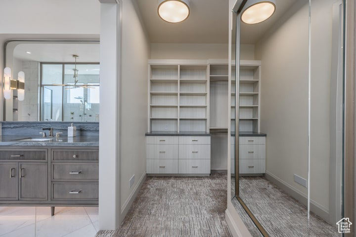 Walk in closet featuring sink, an inviting chandelier, and light tile floors