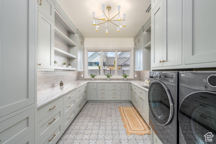 Laundry area with cabinets, light tile floors, washing machine and clothes dryer, and a chandelier