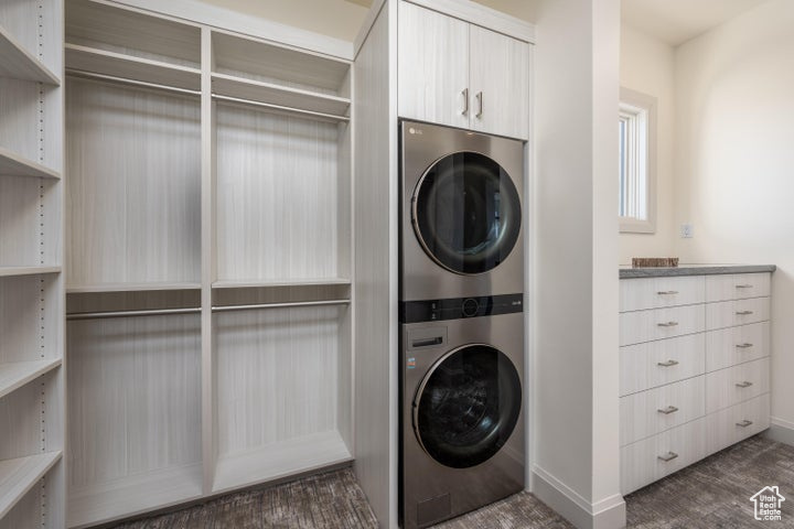 Laundry area with stacked washer and clothes dryer and dark wood-type flooring