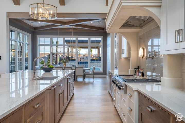 Kitchen featuring light stone counters, white cabinetry, hanging light fixtures, an inviting chandelier, and light wood-type flooring