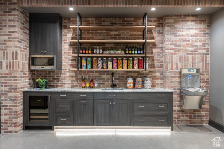 Bar with brick wall, stainless steel microwave, light stone countertops, and sink