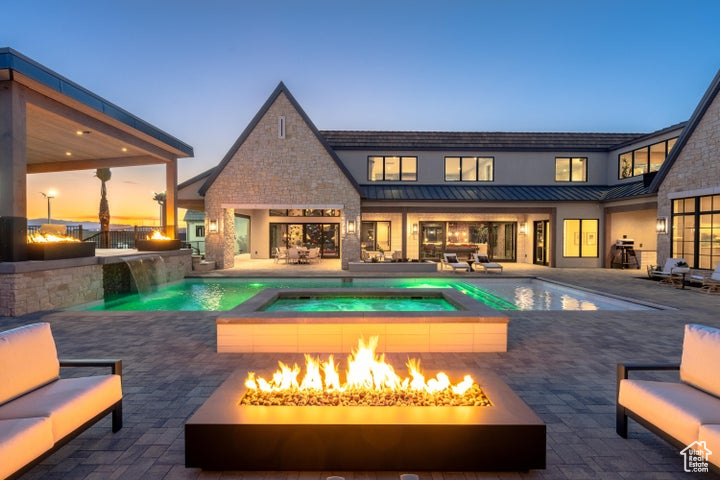 Pool at dusk featuring pool water feature, a patio area, an in ground hot tub, and an outdoor living space with a fire pit