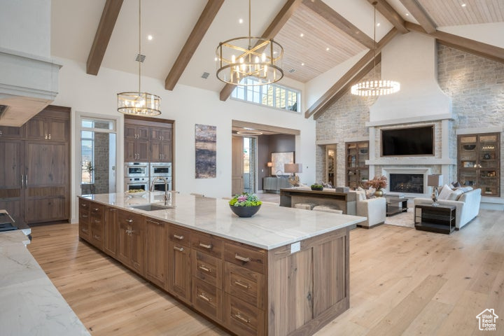 Kitchen featuring high vaulted ceiling, a kitchen island with sink, decorative light fixtures, light wood-type flooring, and an inviting chandelier