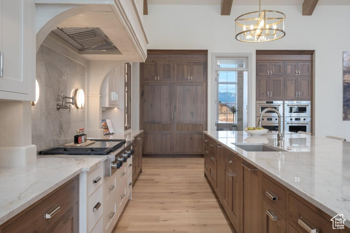 Kitchen featuring white cabinets, light hardwood / wood-style floors, hanging light fixtures, beamed ceiling, and light stone counters