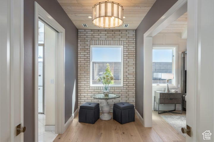 Hallway with brick wall, light hardwood / wood-style floors, and wood ceiling
