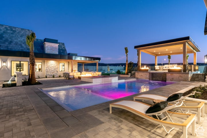 Pool at dusk featuring area for grilling, a patio, and pool water feature