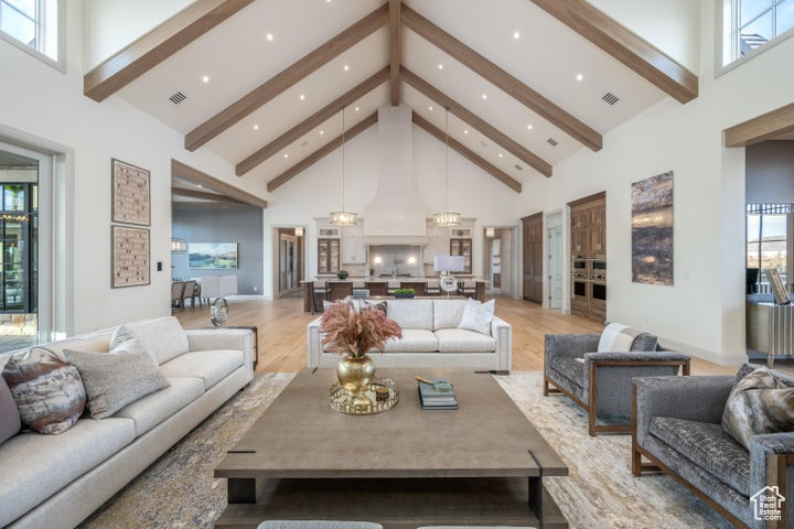 Living room featuring an inviting chandelier, light hardwood / wood-style flooring, beam ceiling, and high vaulted ceiling