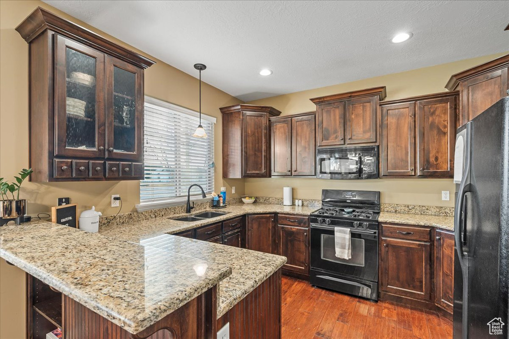 Kitchen featuring light stone countertops, black appliances, pendant lighting, sink, and dark hardwood / wood-style floors