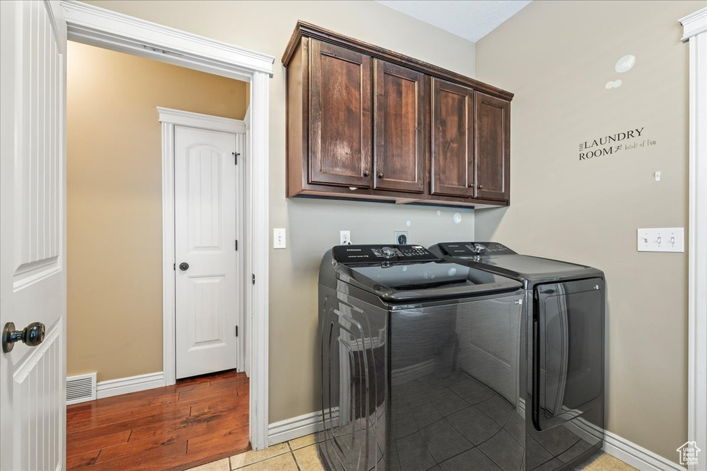 Washroom with cabinets, washer and dryer, and light hardwood / wood-style floors