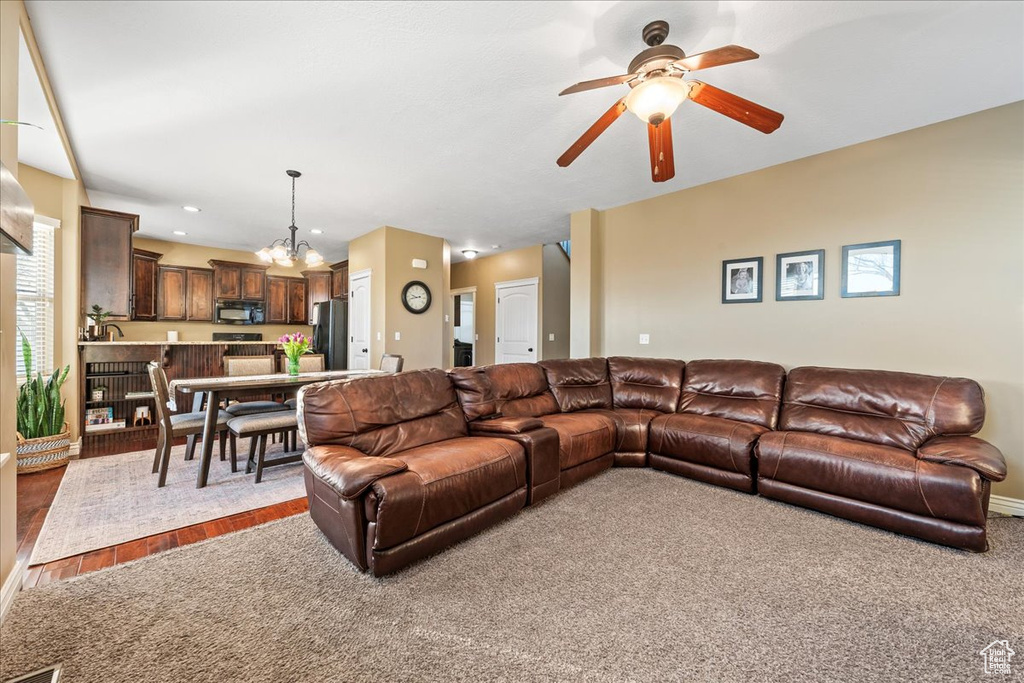 Living room featuring ceiling fan with notable chandelier and carpet flooring