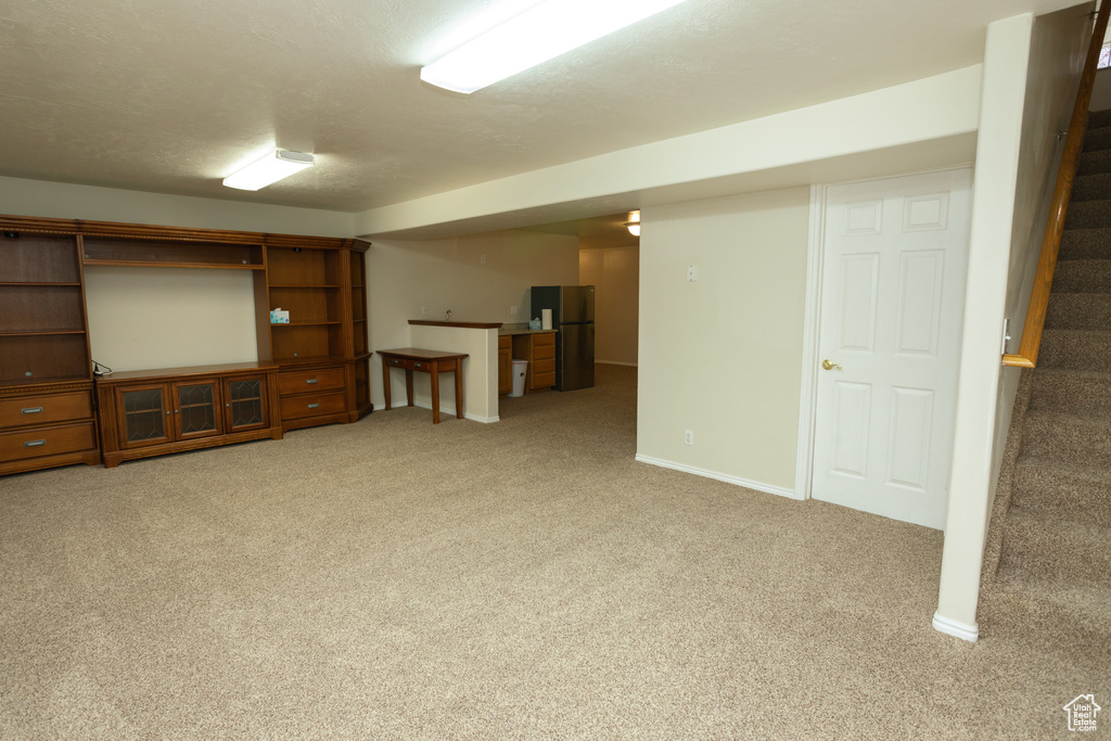 Basement with stainless steel fridge and light carpet