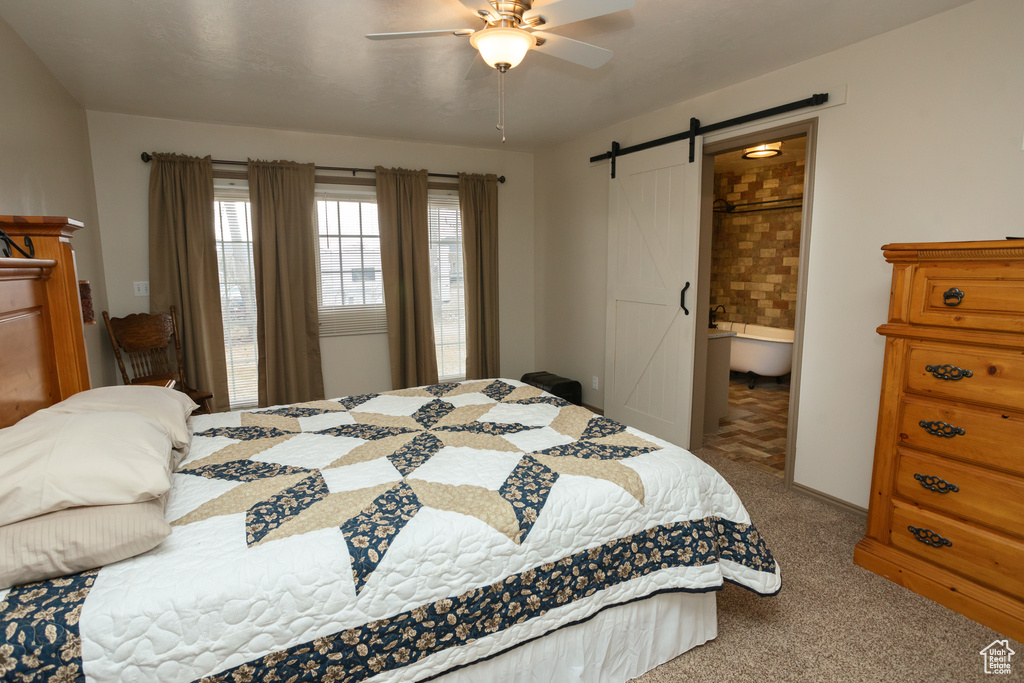 Carpeted bedroom featuring a barn door, ceiling fan, and ensuite bathroom