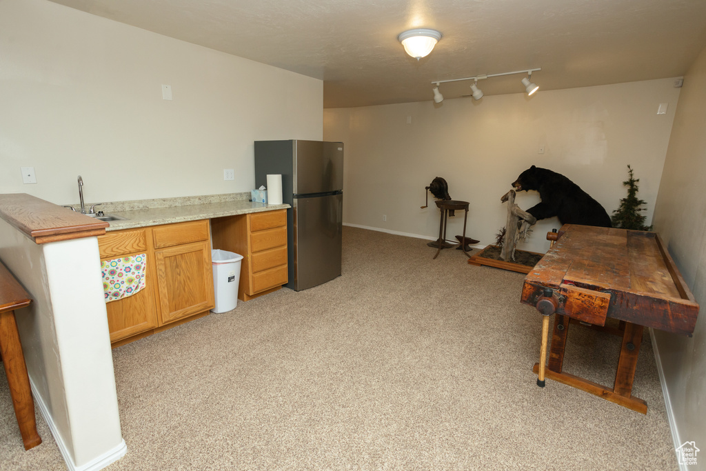 Interior space featuring sink, light colored carpet, stainless steel refrigerator, and track lighting