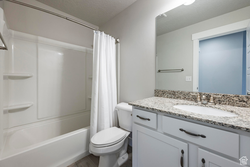Full bathroom with hardwood / wood-style flooring, a textured ceiling, shower / bath combo with shower curtain, toilet, and vanity