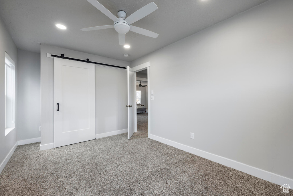 Unfurnished bedroom with a barn door, light carpet, and ceiling fan