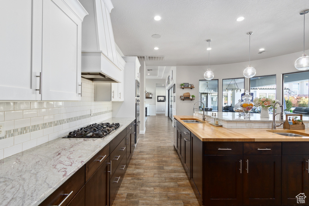 Kitchen featuring white cabinetry, premium range hood, backsplash, and pendant lighting