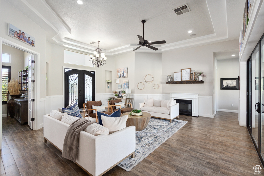 Living room with dark hardwood / wood-style flooring, a raised ceiling, and ceiling fan with notable chandelier