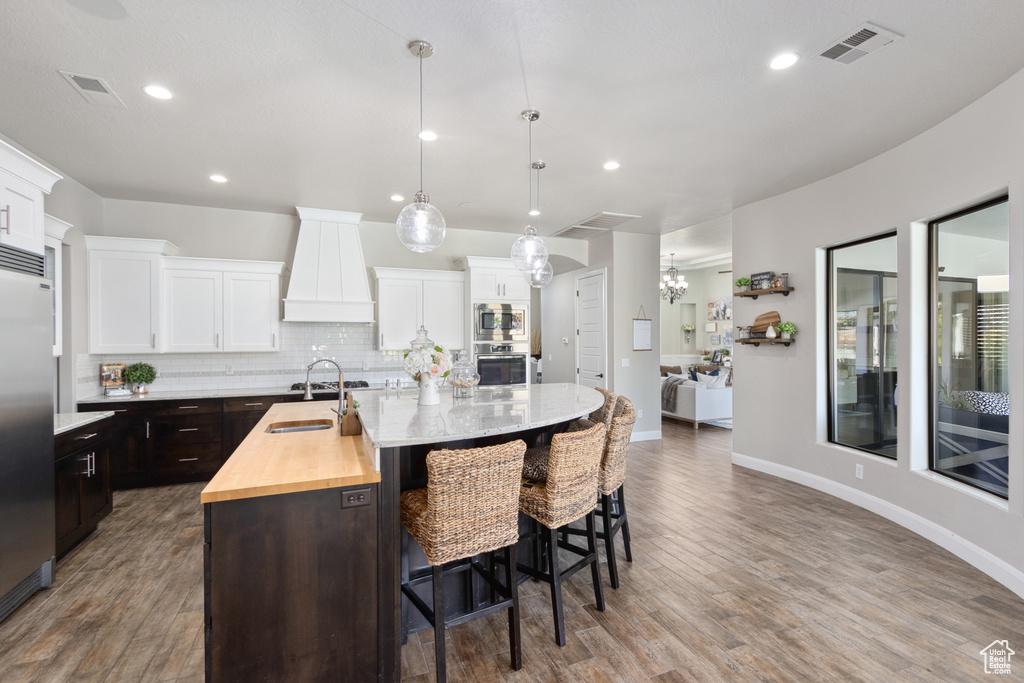 Kitchen featuring backsplash, a kitchen island with sink, hanging light fixtures, custom exhaust hood, and hardwood / wood-style floors