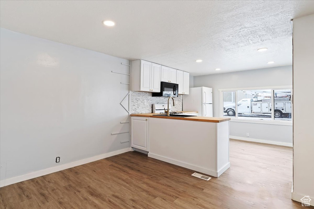Kitchen featuring light wood-type flooring, white cabinets, tasteful backsplash, sink, and white refrigerator