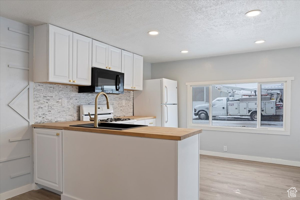 Kitchen with white appliances, light hardwood / wood-style floors, backsplash, and white cabinetry