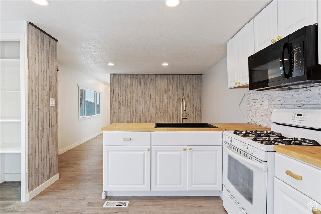 Kitchen featuring light wood-type flooring, white gas range oven, white cabinetry, kitchen peninsula, and sink