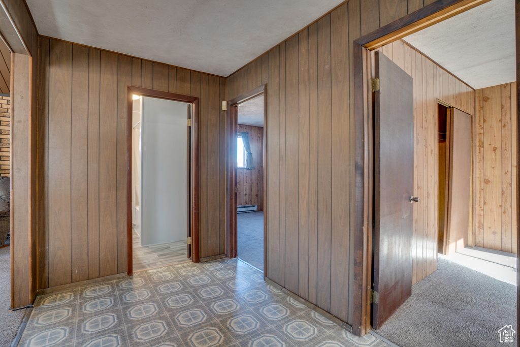 Hall with baseboard heating, wood walls, and light carpet