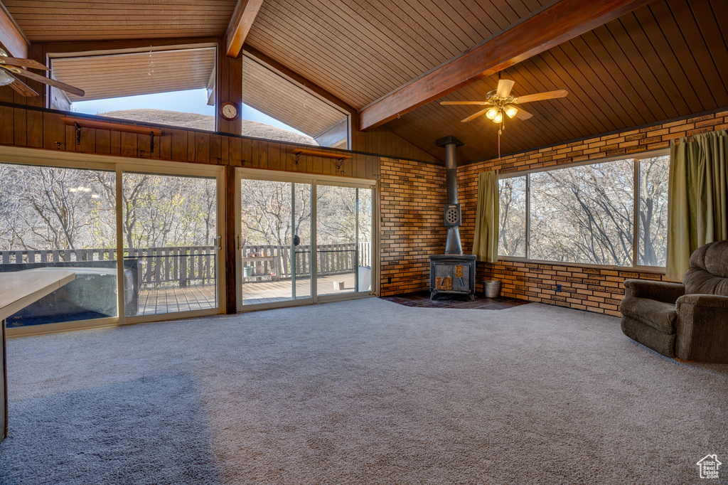 Unfurnished sunroom featuring wood ceiling, plenty of natural light, ceiling fan, and a wood stove