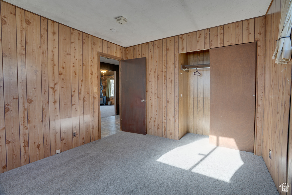 Unfurnished bedroom with light colored carpet, wood walls, and a closet