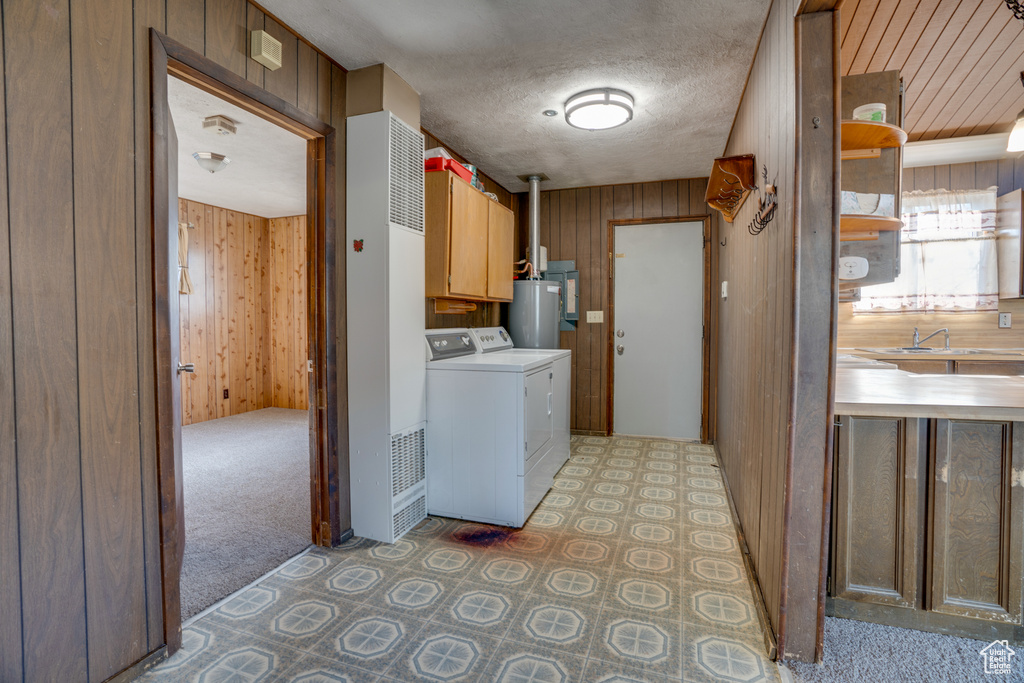 Laundry room featuring separate washer and dryer, light carpet, water heater, wooden walls, and cabinets