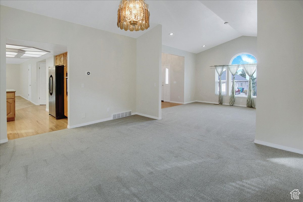 Unfurnished room with lofted ceiling, light colored carpet, and a notable chandelier
