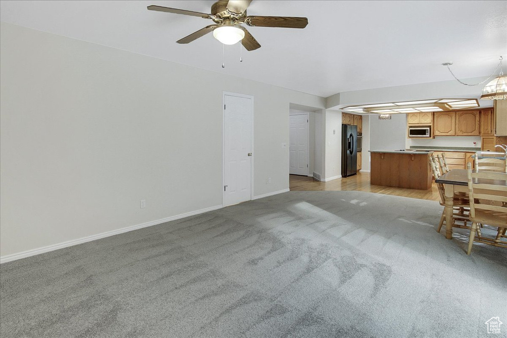 Unfurnished living room featuring sink, ceiling fan, and light carpet