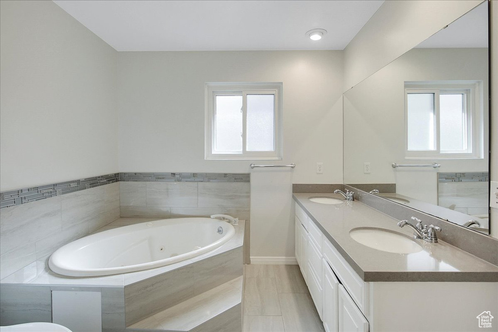 Bathroom with a wealth of natural light, tile floors, double sink vanity, and a relaxing tiled bath