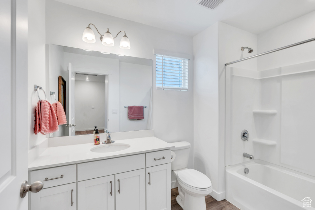 Full bathroom with washtub / shower combination, toilet, hardwood / wood-style floors, and vanity with extensive cabinet space