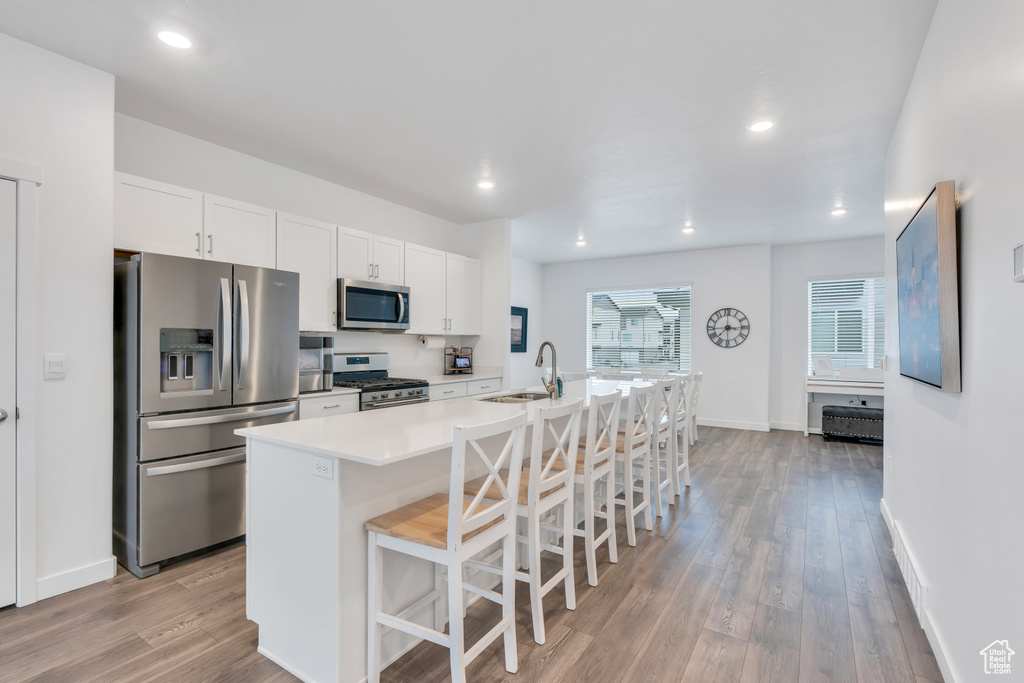 Kitchen featuring stainless steel appliances, a kitchen bar, white cabinetry, light hardwood / wood-style flooring, and an island with sink