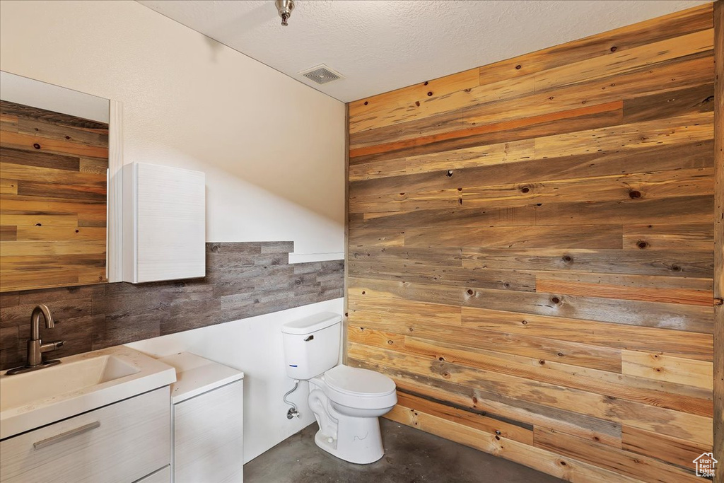 Bathroom with concrete floors, a textured ceiling, vanity, toilet, and wooden walls
