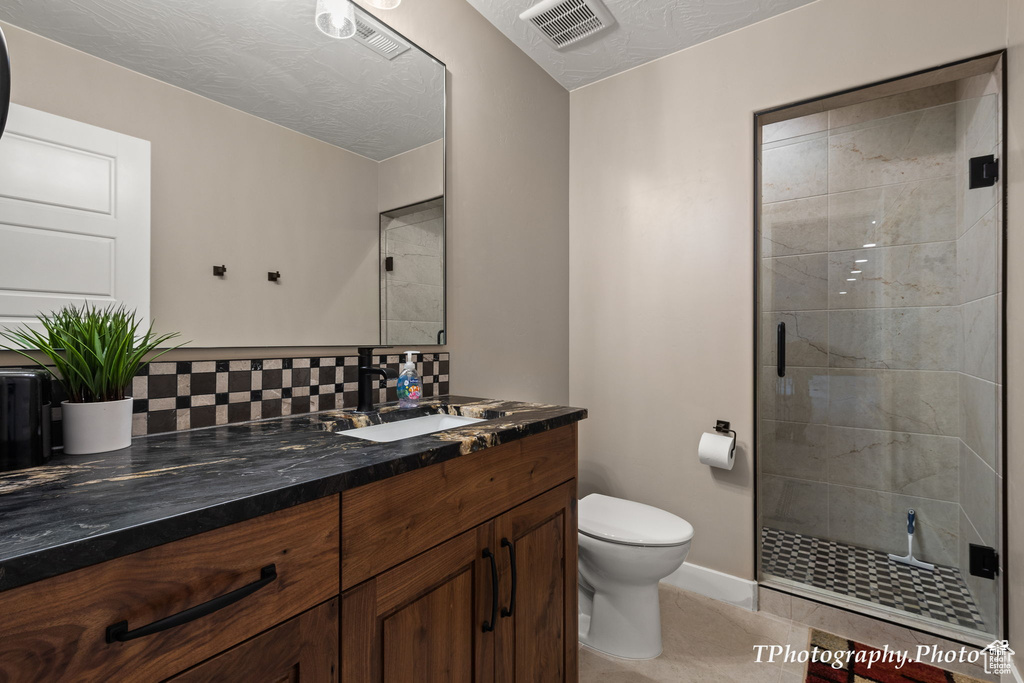 Bathroom with vanity with extensive cabinet space, an enclosed shower, tile flooring, and toilet