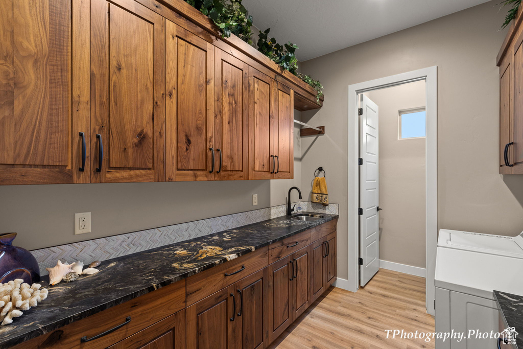 Kitchen featuring light hardwood / wood-style floors, washer and clothes dryer, dark stone counters, and sink