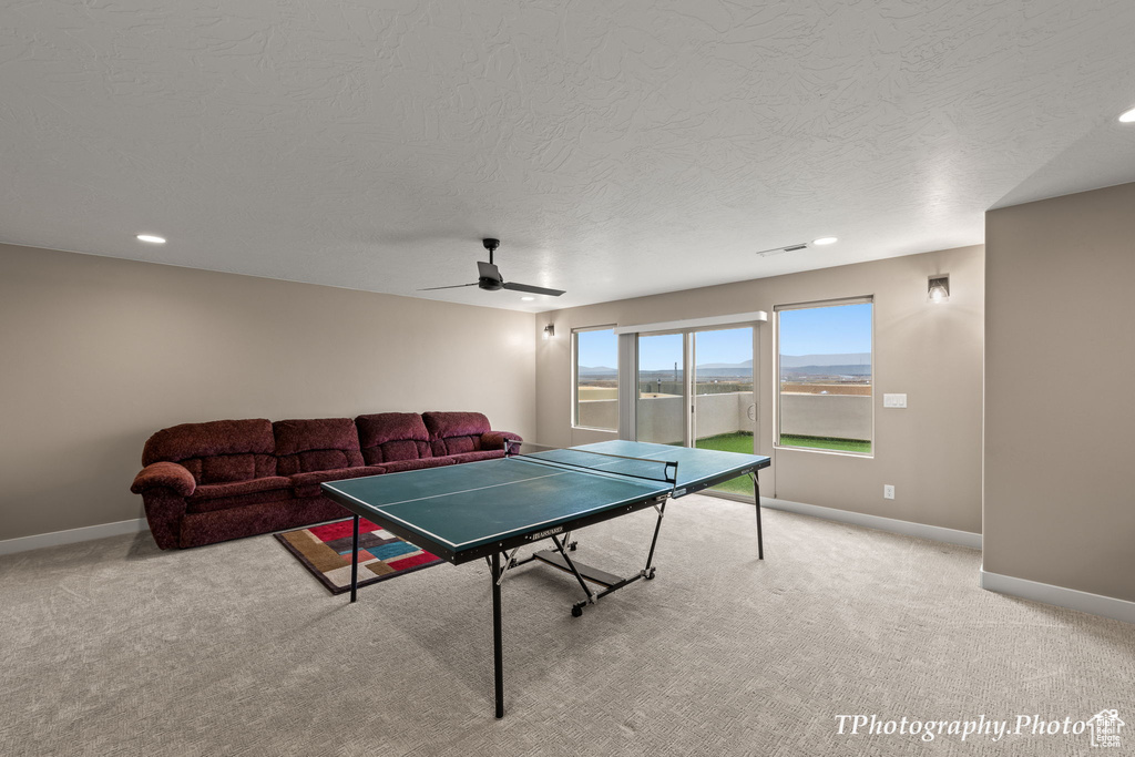 Rec room with ceiling fan, a textured ceiling, and light carpet