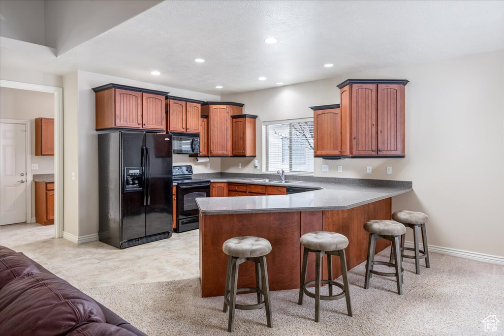 Kitchen featuring kitchen peninsula, a kitchen breakfast bar, sink, black appliances, and light tile floors