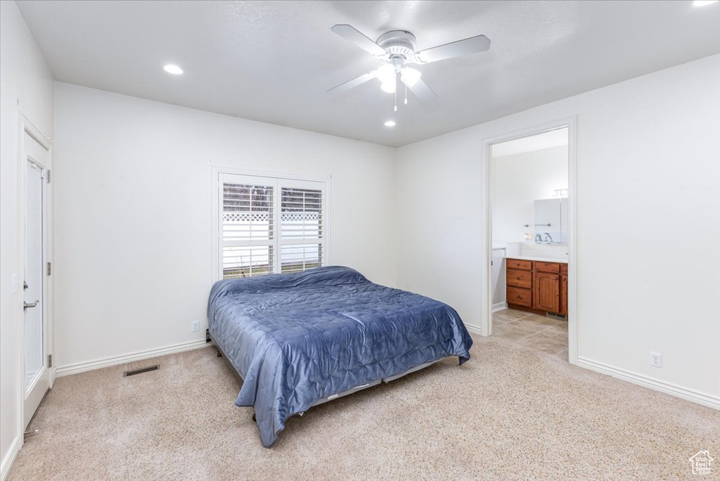 Bedroom with ensuite bathroom, ceiling fan, and light colored carpet