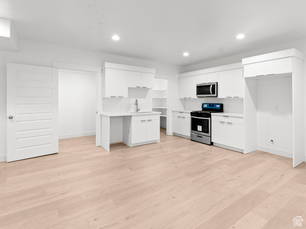 Kitchen featuring light hardwood / wood-style flooring, stainless steel appliances, tasteful backsplash, and white cabinetry