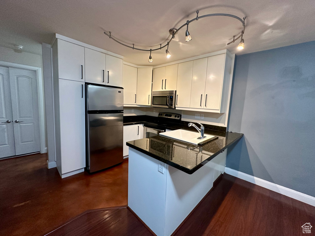 Kitchen featuring rail lighting, kitchen peninsula, white cabinetry, and stainless steel appliances