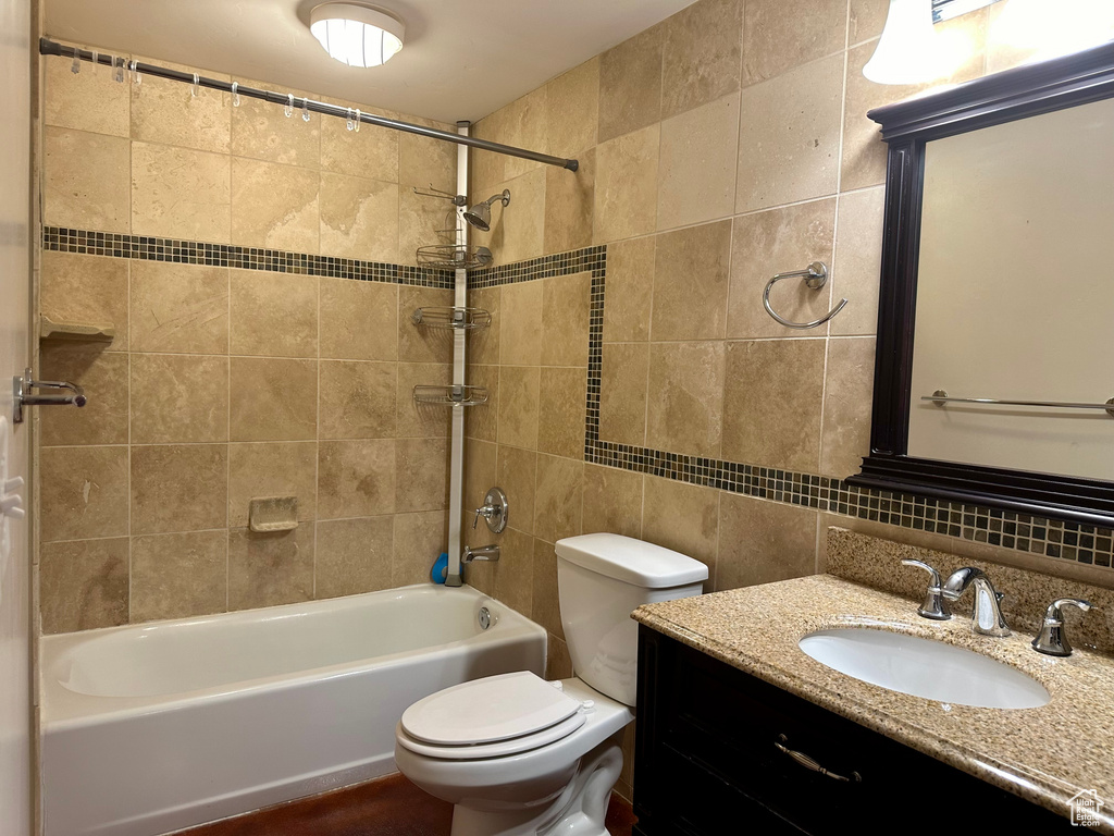 Full bathroom with tiled shower / bath, tile walls, backsplash, toilet, and vanity
