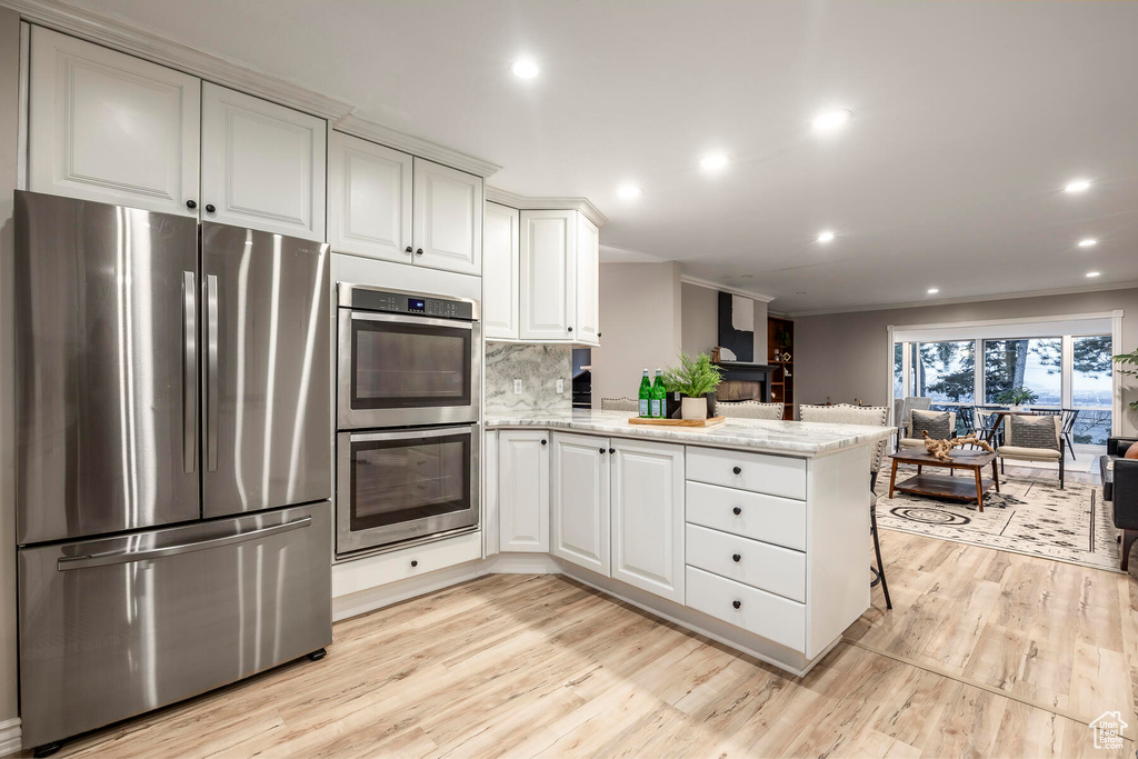 Kitchen with tasteful backsplash, appliances with stainless steel finishes, light stone countertops, and light wood-type flooring